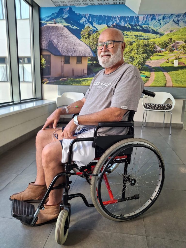 Jean sitting in a wheelchair at the hospital, smiling despite severe gout pain